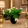 Artificial flower arrangement in a black vase on a marble surface with decorative elements.